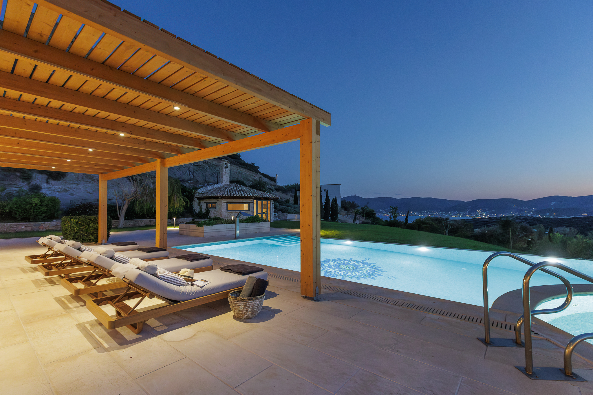 Pergola-shaded training deck beside the heated infinity pool at Villa Lithos Porto Rafti at dusk